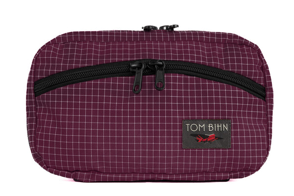 The front of a Handy Little Thing #2 in Acai (purple with white grid) 200 Halcyon showing the front zipper with two slider and logo at the bottom-right corner.
